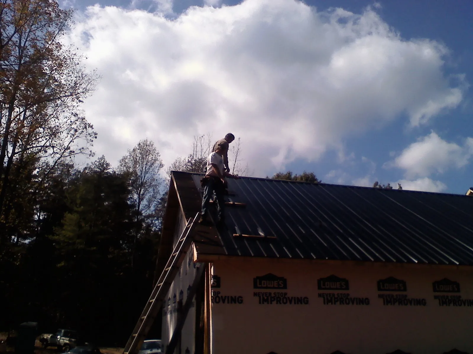 Roofer fastening dark metal panels high against a cloudy sky, from a Roof Inspection job in Audubon