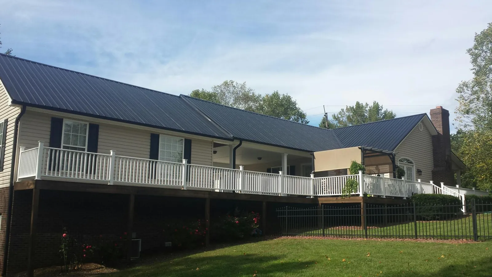 Black metal roof above a long white railed deck on a hillside home in Audubon