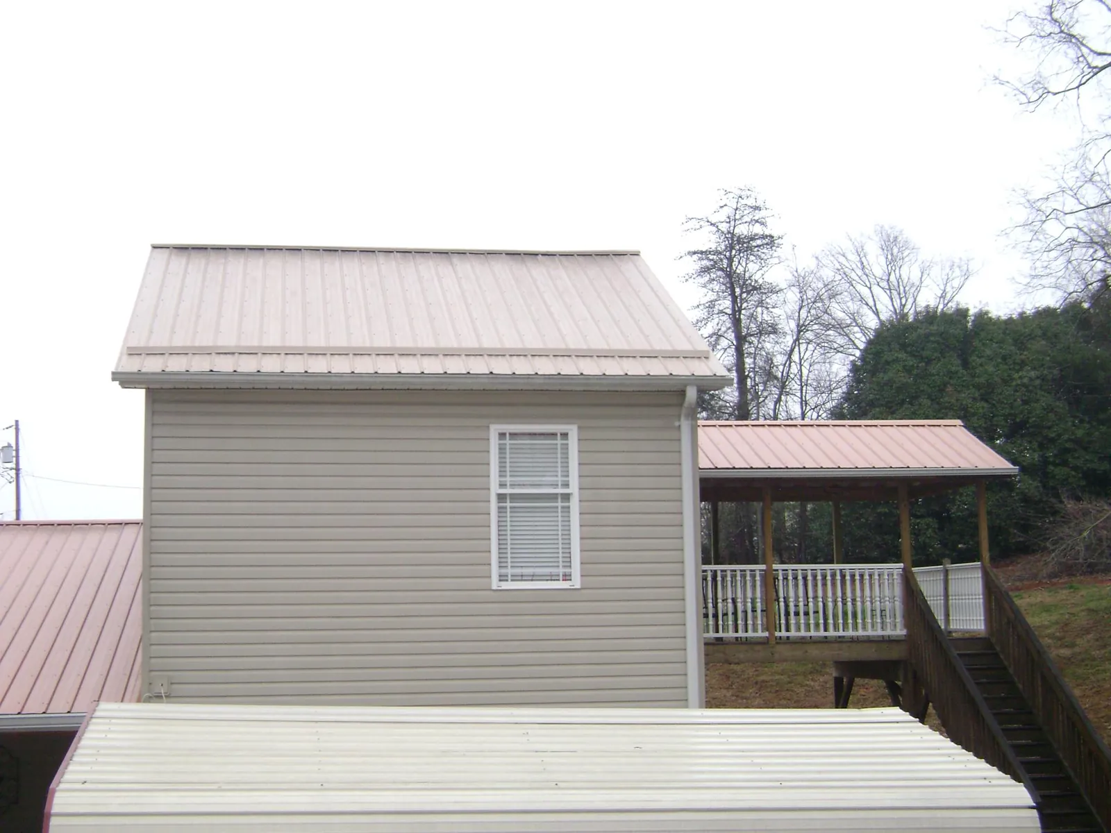 Tan metal roofs on a two story addition and attached porch, from a Roof Replacement job in Audubon